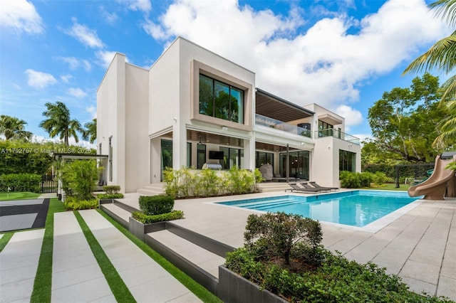 back of house with fence, stucco siding, a fenced in pool, a balcony, and a patio
