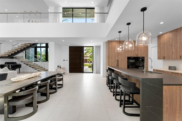 bar with dobule oven black, stairs, a towering ceiling, light tile patterned flooring, and a sink