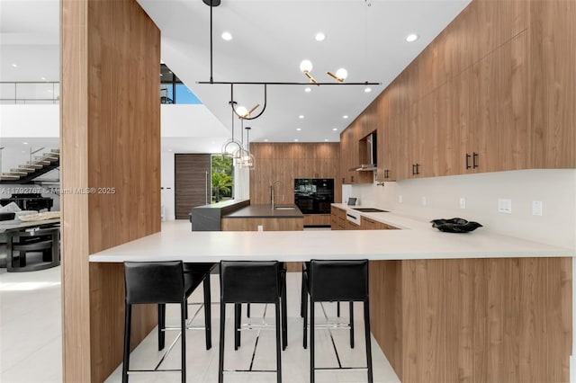 kitchen with modern cabinets, brown cabinets, a sink, a peninsula, and a breakfast bar