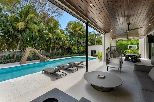 outdoor pool with a patio, a fenced backyard, ceiling fan, and a water slide