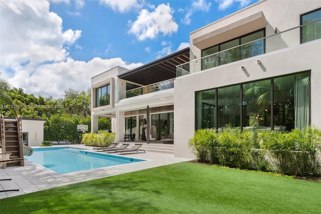 back of property with a yard, a patio area, stucco siding, and a balcony