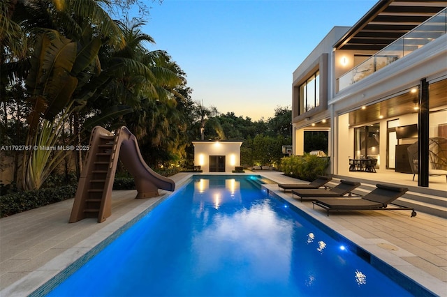 outdoor pool with a water slide and a patio area