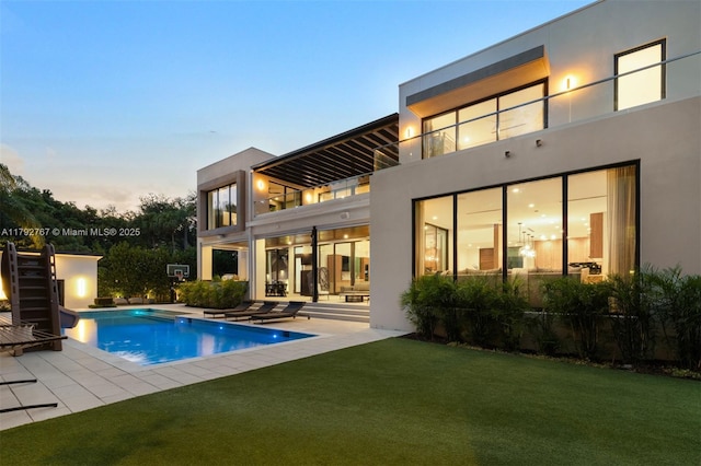back of property with stucco siding, an outdoor pool, a balcony, a patio, and a yard