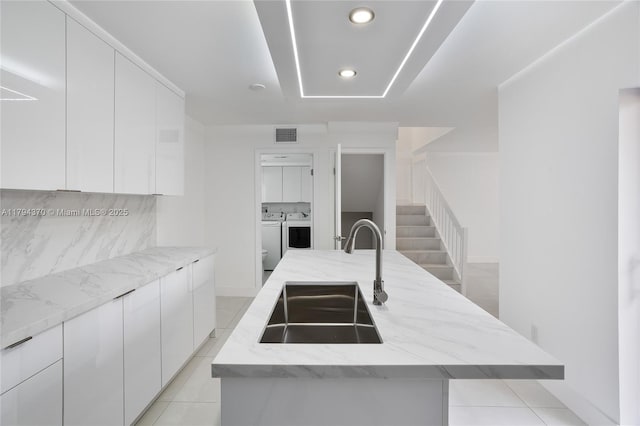 853 SW 118th Ter, Davie, FL 33325 - kitchen with light stone countertops, modern cabinets, a center island with sink, separate washer and dryer, and a sink