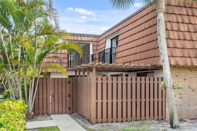 853 SW 118th Ter, Davie, FL 33325 - view of property exterior with a fenced front yard, a gate, brick siding, mansard roof, and a balcony