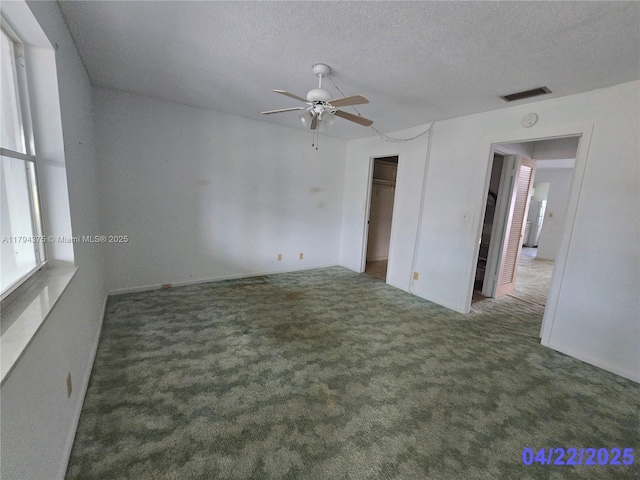 carpeted spare room with a textured ceiling, ceiling fan, and visible vents