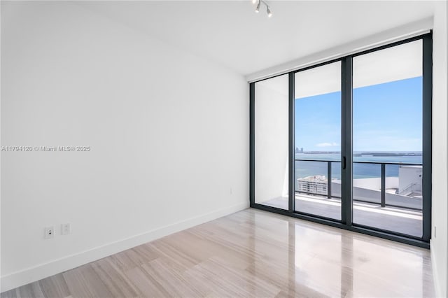 spare room with baseboards, floor to ceiling windows, and a water view