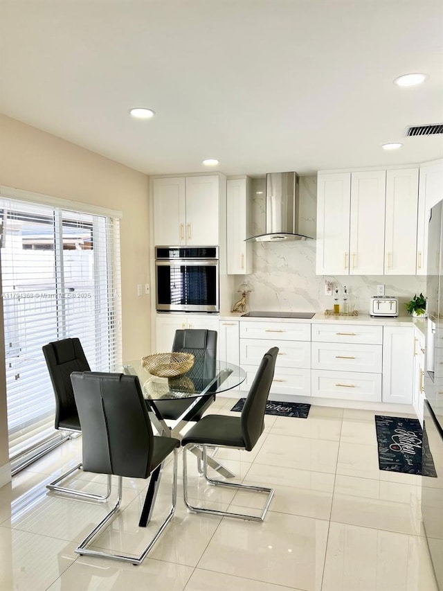 kitchen featuring wall chimney range hood, oven, white cabinets, and light countertops