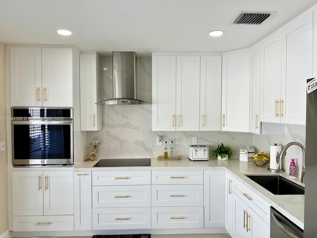 kitchen featuring visible vents, wall chimney exhaust hood, white cabinetry, a sink, and stainless steel appliances