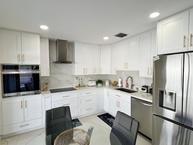 kitchen with visible vents, wall chimney range hood, white cabinets, a sink, and stainless steel appliances
