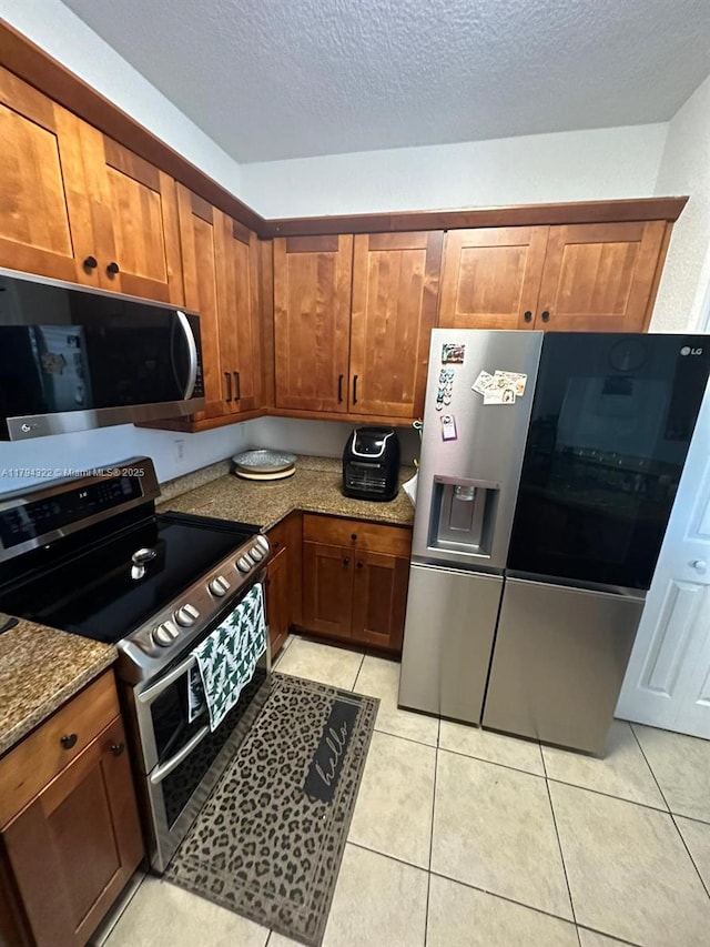 kitchen with dark stone counters, brown cabinets, appliances with stainless steel finishes, and light tile patterned floors