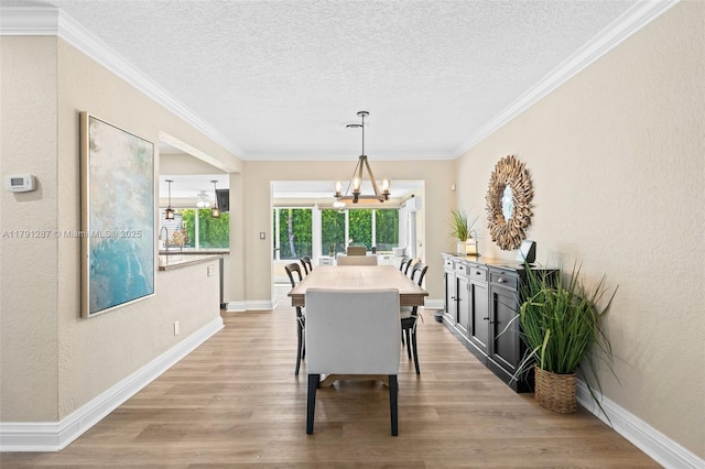 dining room with crown molding, a textured ceiling, a notable chandelier, and light wood-style floors