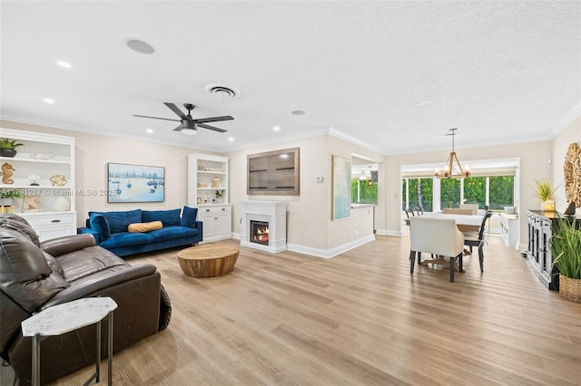 living room with visible vents, light wood finished floors, ceiling fan with notable chandelier, and a lit fireplace