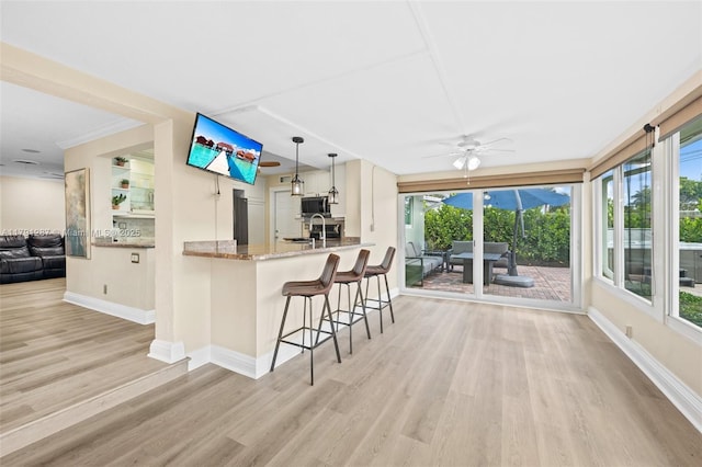 kitchen featuring baseboards, light wood-type flooring, stainless steel microwave, light stone counters, and a wealth of natural light