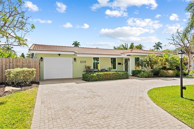 view of front of property featuring fence, an attached garage, a tile roof, stucco siding, and decorative driveway