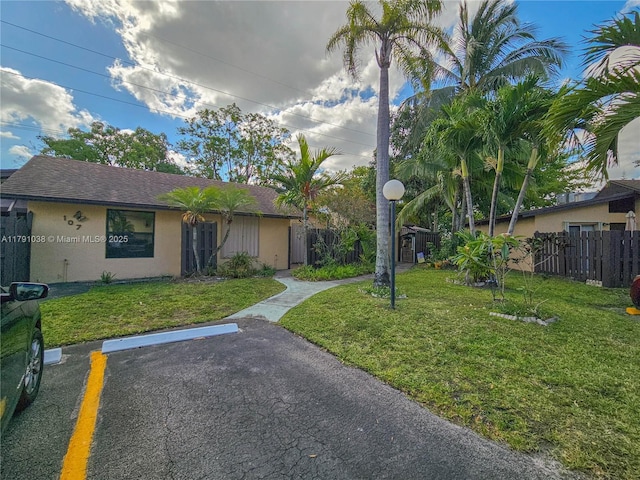 view of front of property featuring fence, stucco siding, uncovered parking, and a front yard