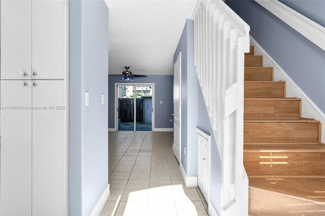 stairs featuring baseboards, tile patterned floors, a textured wall, and ceiling fan