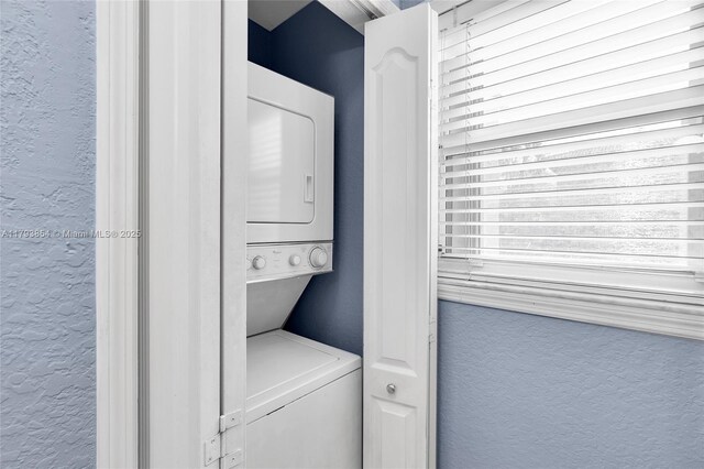 washroom featuring laundry area, stacked washer and dryer, and a textured wall