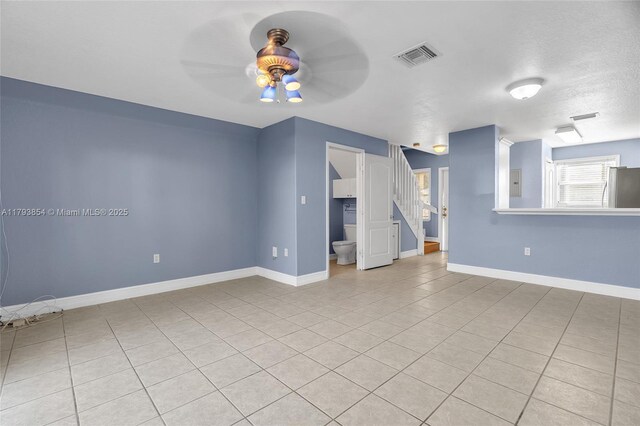 spare room with ceiling fan, visible vents, light tile patterned floors, baseboards, and stairs