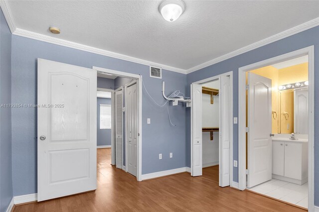 unfurnished bedroom with visible vents, ornamental molding, baseboards, and wood finished floors