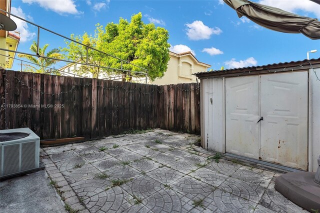 view of patio with an outdoor structure, cooling unit, a fenced backyard, and a shed