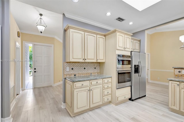 kitchen with cream cabinets, crown molding, appliances with stainless steel finishes, light wood finished floors, and backsplash