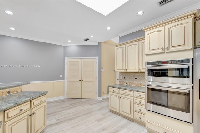kitchen with visible vents, wainscoting, double oven, ornamental molding, and cream cabinetry