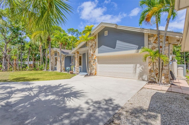 view of front of home featuring a garage, a front lawn, stone siding, and concrete driveway