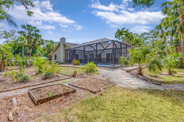 rear view of house with a garden, a chimney, glass enclosure, a yard, and stucco siding