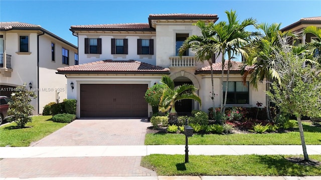 mediterranean / spanish-style house featuring a garage, stucco siding, a tile roof, and decorative driveway
