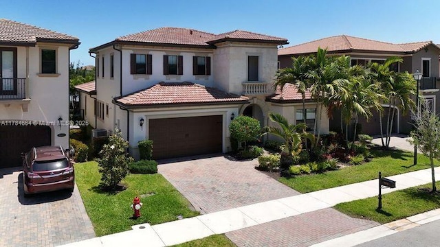 mediterranean / spanish-style home with stucco siding, an attached garage, a tile roof, and decorative driveway