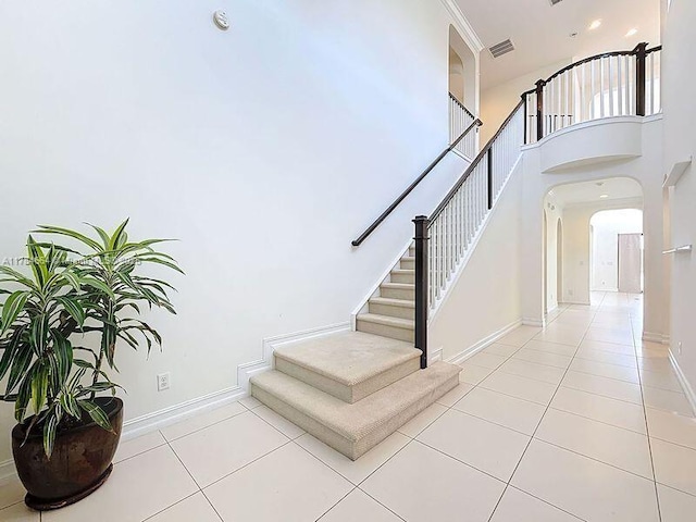 stairway with arched walkways, tile patterned floors, visible vents, and baseboards