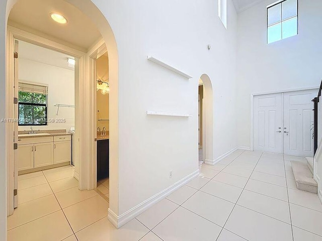 hall featuring a high ceiling, a sink, arched walkways, baseboards, and light tile patterned floors