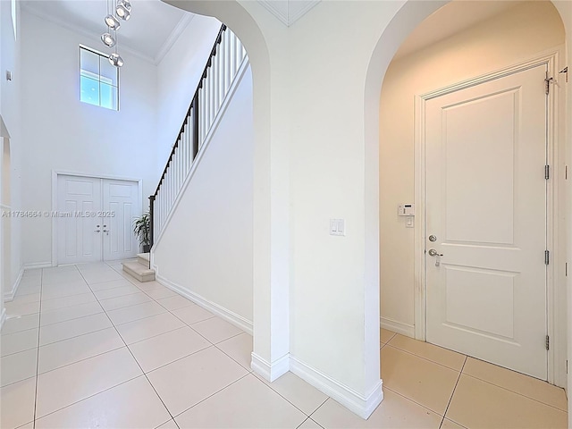 foyer entrance with arched walkways, baseboards, ornamental molding, and light tile patterned floors