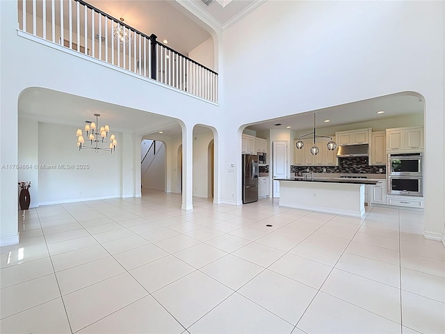 unfurnished living room with crown molding, a notable chandelier, arched walkways, light tile patterned floors, and a towering ceiling