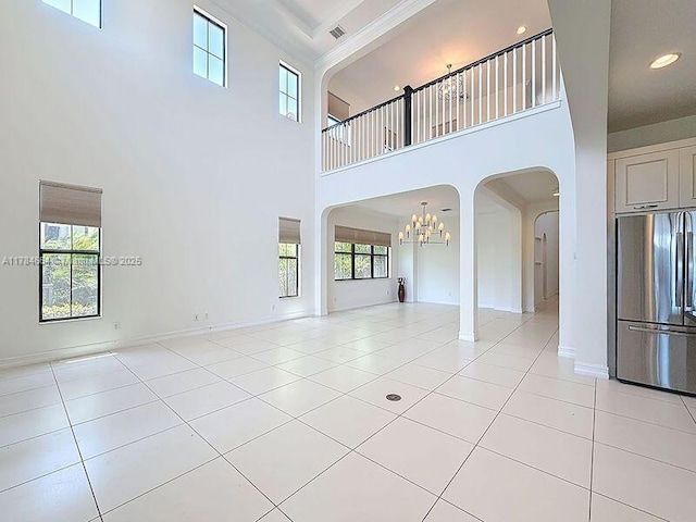 unfurnished living room with arched walkways, a notable chandelier, light tile patterned flooring, and a towering ceiling