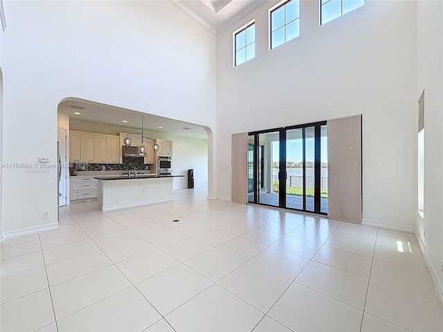 unfurnished living room with light tile patterned floors, arched walkways, baseboards, and a towering ceiling