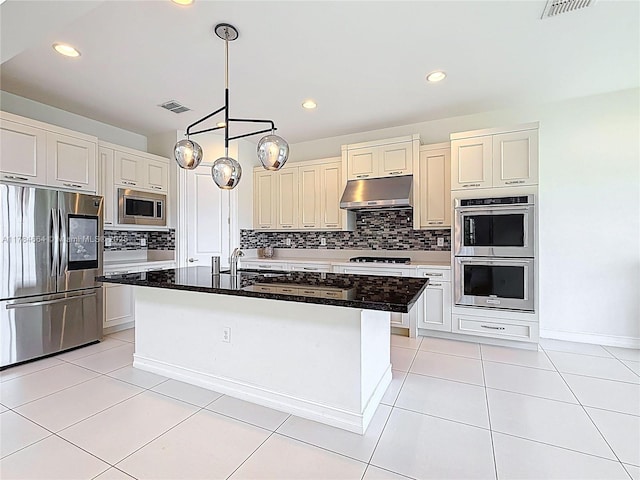 kitchen with appliances with stainless steel finishes, tasteful backsplash, under cabinet range hood, visible vents, and a center island with sink
