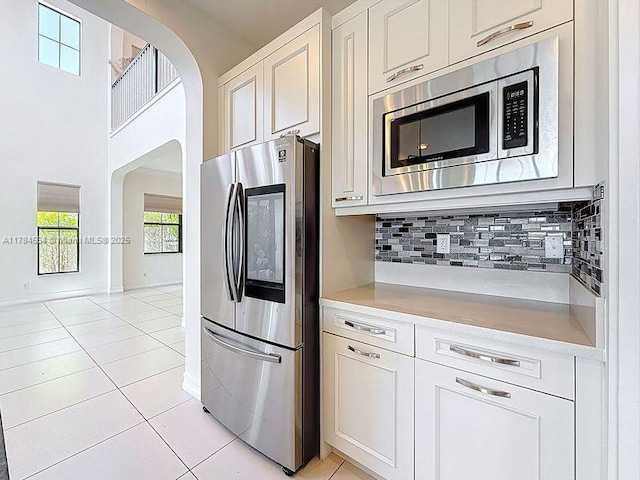 kitchen featuring decorative backsplash, arched walkways, light tile patterned floors, light countertops, and stainless steel appliances