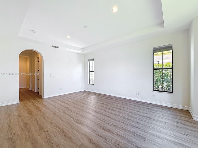 unfurnished room featuring arched walkways, baseboards, a tray ceiling, and wood finished floors