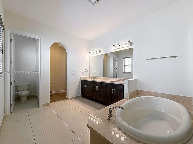 full bathroom featuring double vanity, a garden tub, a sink, tile patterned floors, and toilet