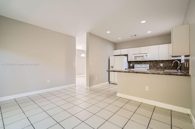 kitchen featuring a peninsula, white appliances, white cabinetry, tasteful backsplash, and a sink