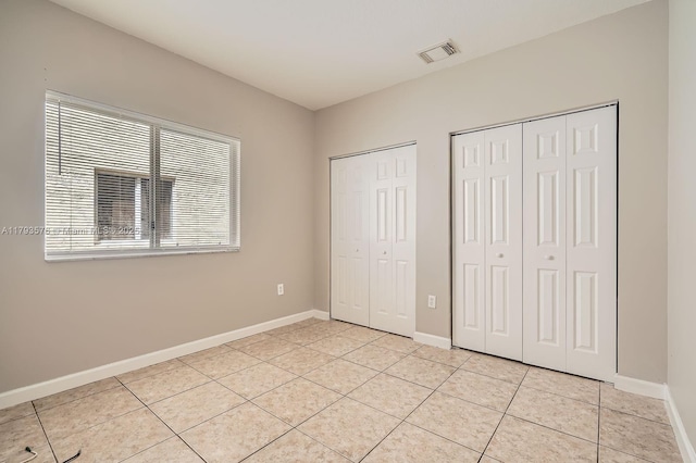 unfurnished bedroom featuring two closets, light tile patterned flooring, baseboards, and visible vents