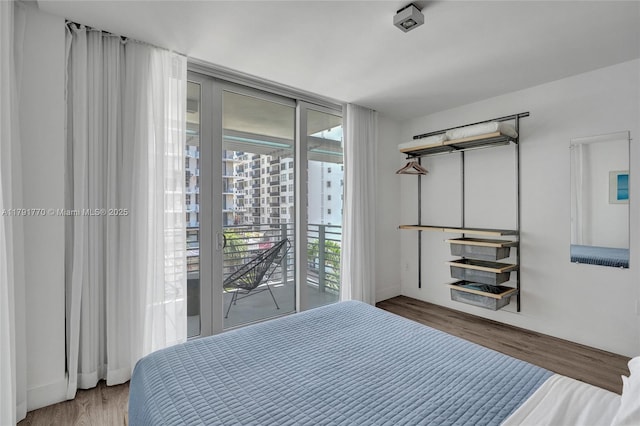 bedroom featuring baseboards, a wall of windows, wood finished floors, and access to exterior