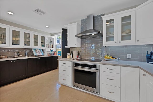 kitchen with visible vents, decorative backsplash, stainless steel oven, wall chimney range hood, and light countertops