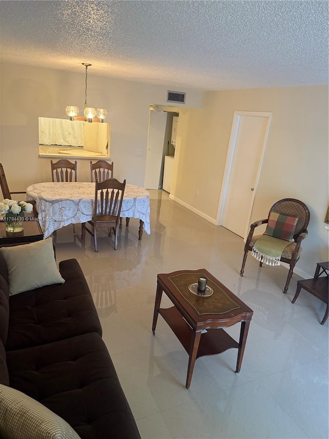 living area featuring a textured ceiling, visible vents, baseboards, and an inviting chandelier