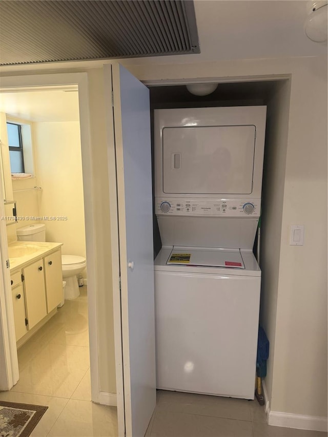 laundry room featuring stacked washing maching and dryer, light tile patterned floors, and baseboards