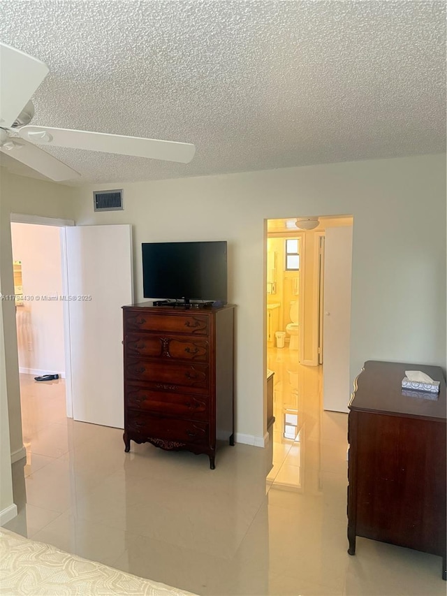 bedroom with connected bathroom, light tile patterned flooring, a textured ceiling, a ceiling fan, and visible vents