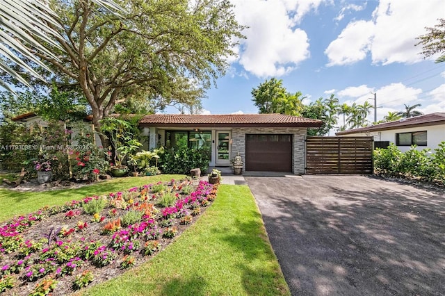 480 NW 88th Ter, El Portal, FL 33150 - ranch-style house featuring stone siding, a garage, a tile roof, fence, and aphalt driveway