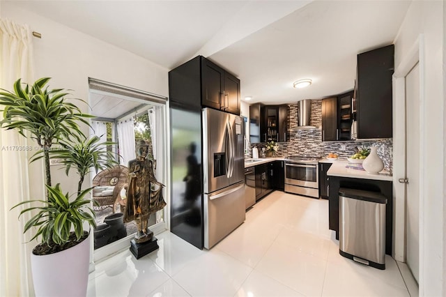 kitchen with backsplash, light countertops, light tile patterned floors, stainless steel appliances, and wall chimney exhaust hood
